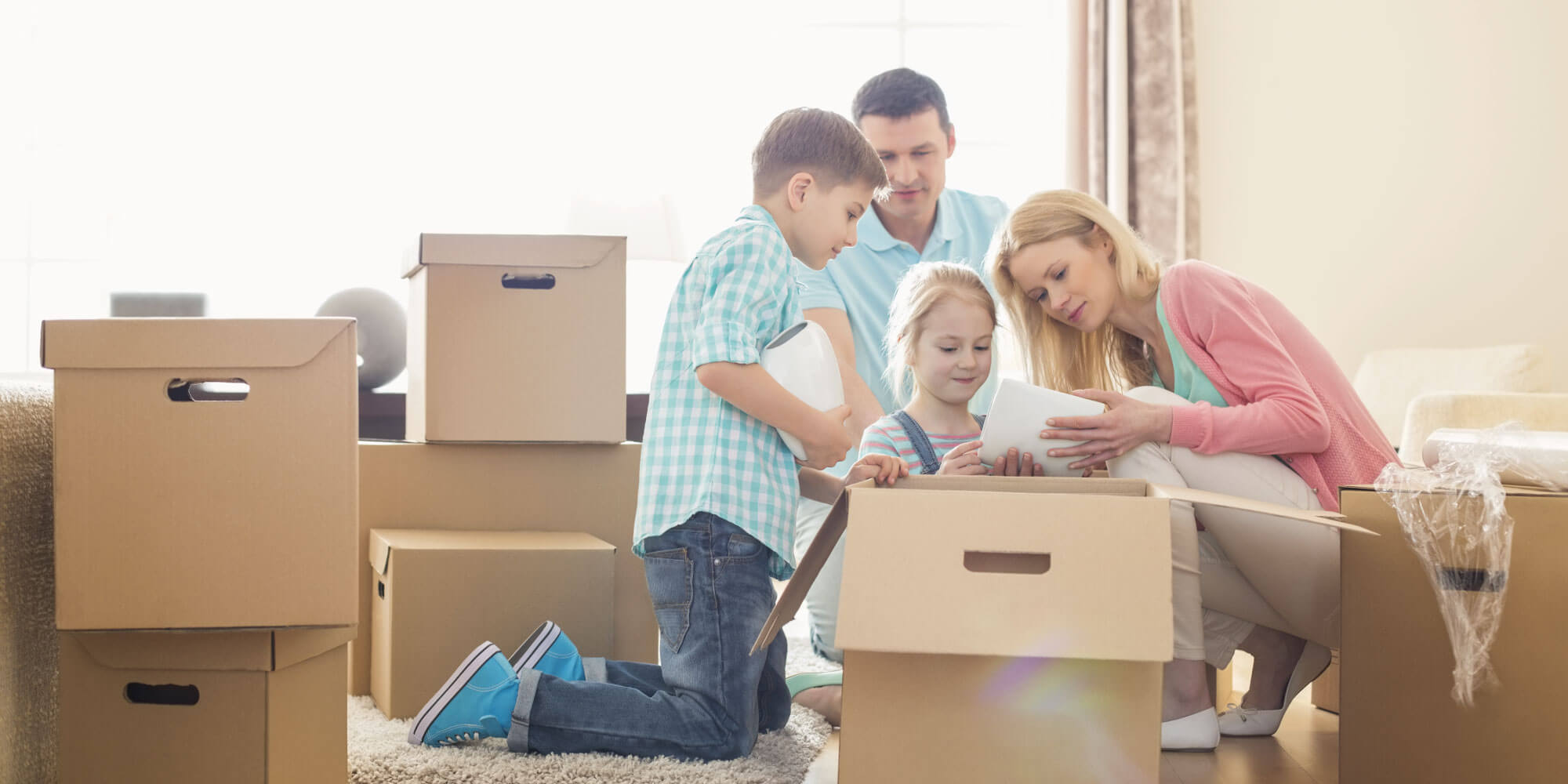 A family of four surrounded by carboard packing boxes in their living room, opening one box together
